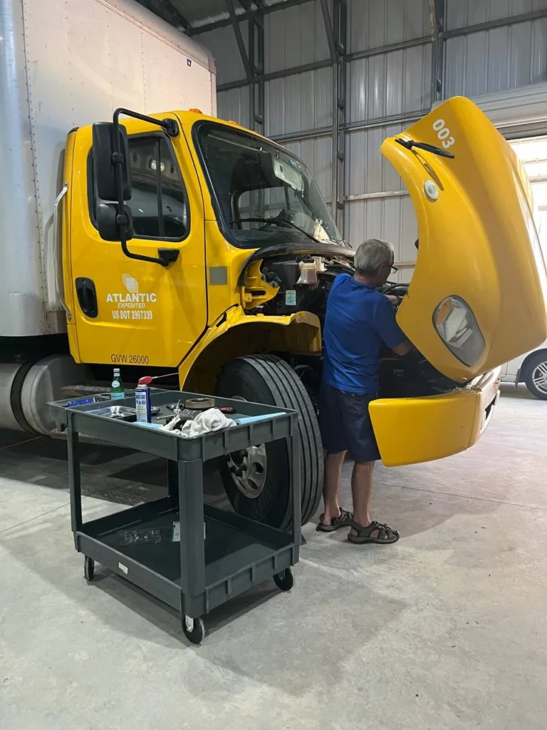 Atlantic Expedited mechanic servicing a box truck engine with the hood raised in the shop